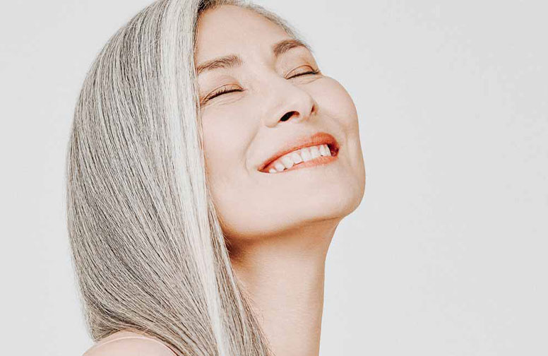 来自亚洲的抗衰老秘诀--白茶! Lächelnde Frau mit grauen Haaren und strahlender Haut, repräsentiert die Anti-Aging-Vorteile von Hautpflegeprodukten mit weißem Tee.